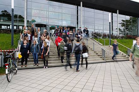 Foto: Studierende stehen auf der Treppe vor dem Universitätsgebäude.