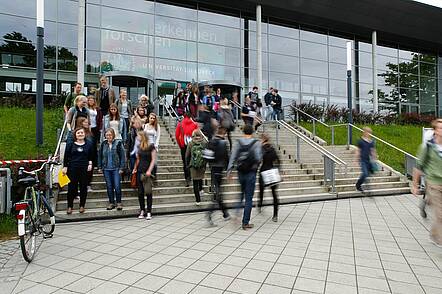 Foto: Studierende stehen auf der Treppe vor dem Universitätsgebäude.