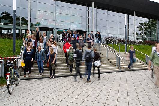 Foto: Studierende stehen auf der Treppe vor dem Universitätsgebäude.