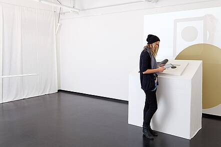 Foto: Eine Studierende des Studiengangs Mediadesign steht in einer Ausstellung vor einem Exponat.