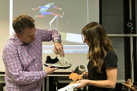 Dozent erläutert einer Studentin Aspekte der Biomechanik am Beispiel eines Fußes im Sportschuh.