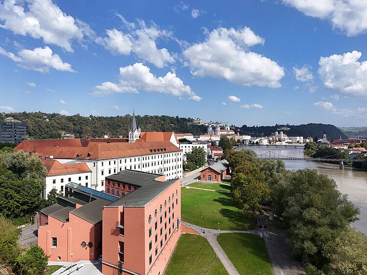 Foto: Blick auf das Hauptgebäude der Universität Passau, im Hintergrund der Fluß Inn, Grünflächen und die Stadt Passau