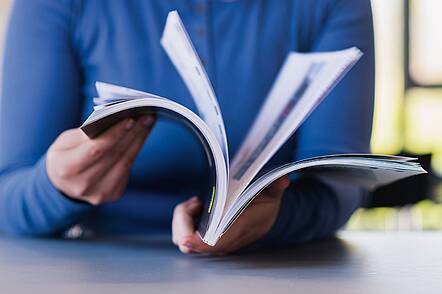 Foto: Eine Studentin mit blauem Pulli durchblättert ein Buch 