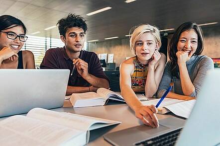 Foto: Studierende sitzen gemeinsam am Schreibtisch und diskutieren Ergebnisse vor Laptop.