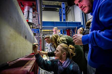 Foto: Studierende arbeiten an einem Versuchsaufbau in einer Technikhalle