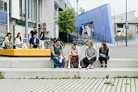 Foto: Studierende sitzen auf dem Campus der Hochschule der Medien Stuttgart und unterhalten sich