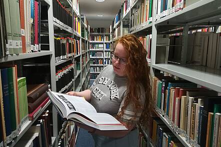 Foto: Eine Studierende der Kirchlichen Hochschule Wuppertal steht in der Bibliothek und blickt in ein Buch